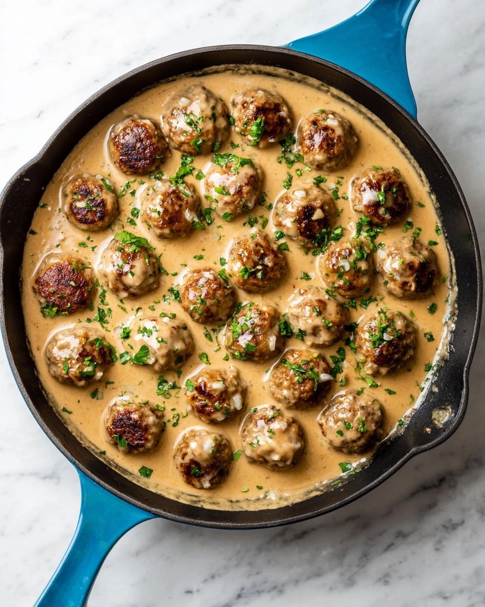A white bowl contains a serving of mashed potatoes on the left side, creamy and smooth with a small well filled with light brown gravy. Five browned Swedish meatballs coated with a light beige sauce are placed on the right side of the mashed potatoes, garnished with small green herbs. Bright green steamed broccolini is neatly arranged on the far right side of the bowl. A small dollop of deep red lingonberry sauce is placed on the edge of the mashed potatoes near the bottom left of the bowl. The bowl sits on a white marbled surface. Photo taken with an iphone --ar 4:5 --v 7