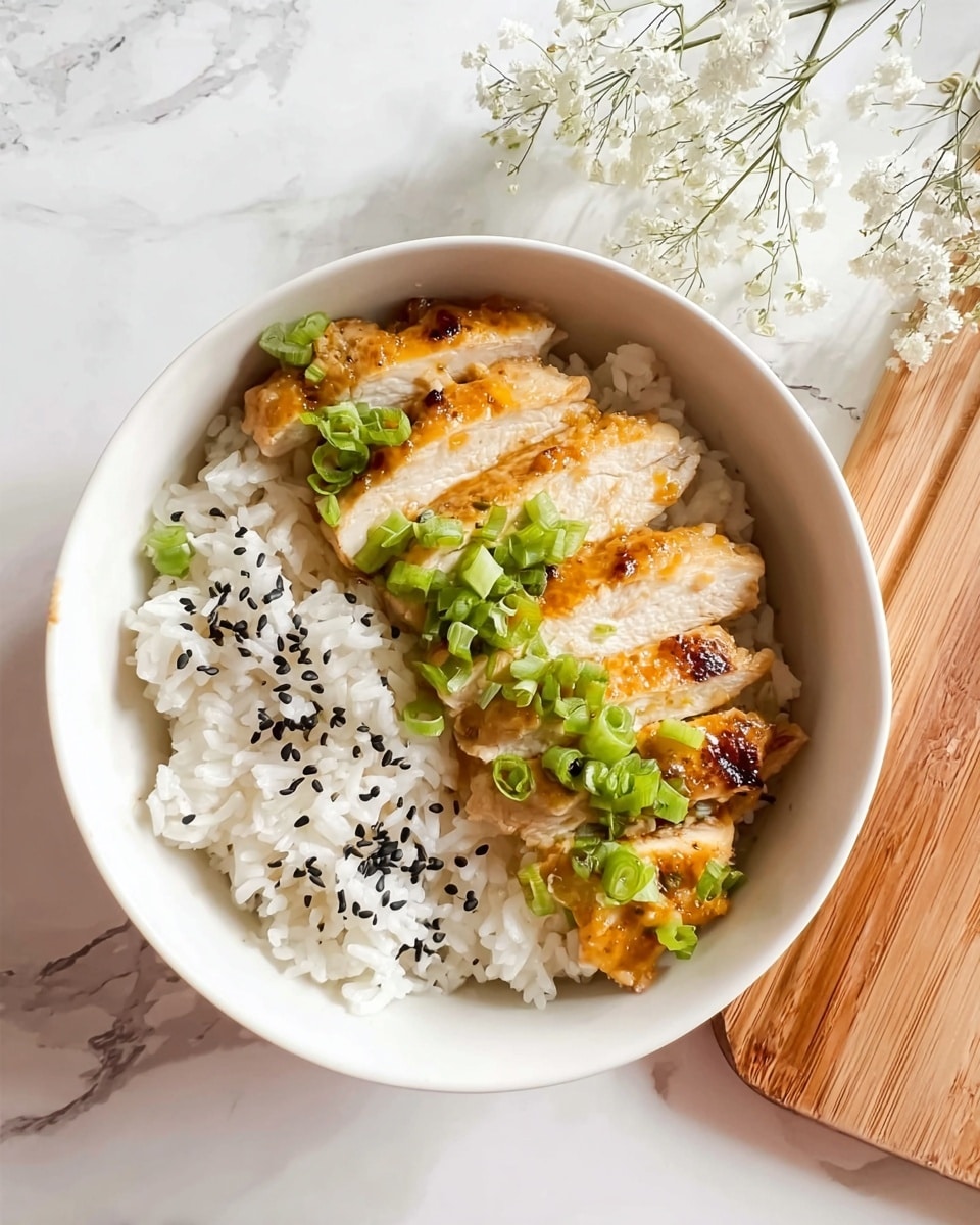 A white bowl holds two main layers: on the left side, there is fluffy white rice topped with scattered black sesame seeds, showing texture in the grains; on the right side, there are five slices of golden-brown cooked chicken laid neatly, each slice with a light char and moist texture, garnished with fresh, bright green chopped scallions spread evenly across the chicken. The bowl is placed on a white marbled surface, with a wooden area visible at the top right corner, and delicate white flowers hanging slightly into the frame above. Photo taken with an iphone --ar 4:5 --v 7