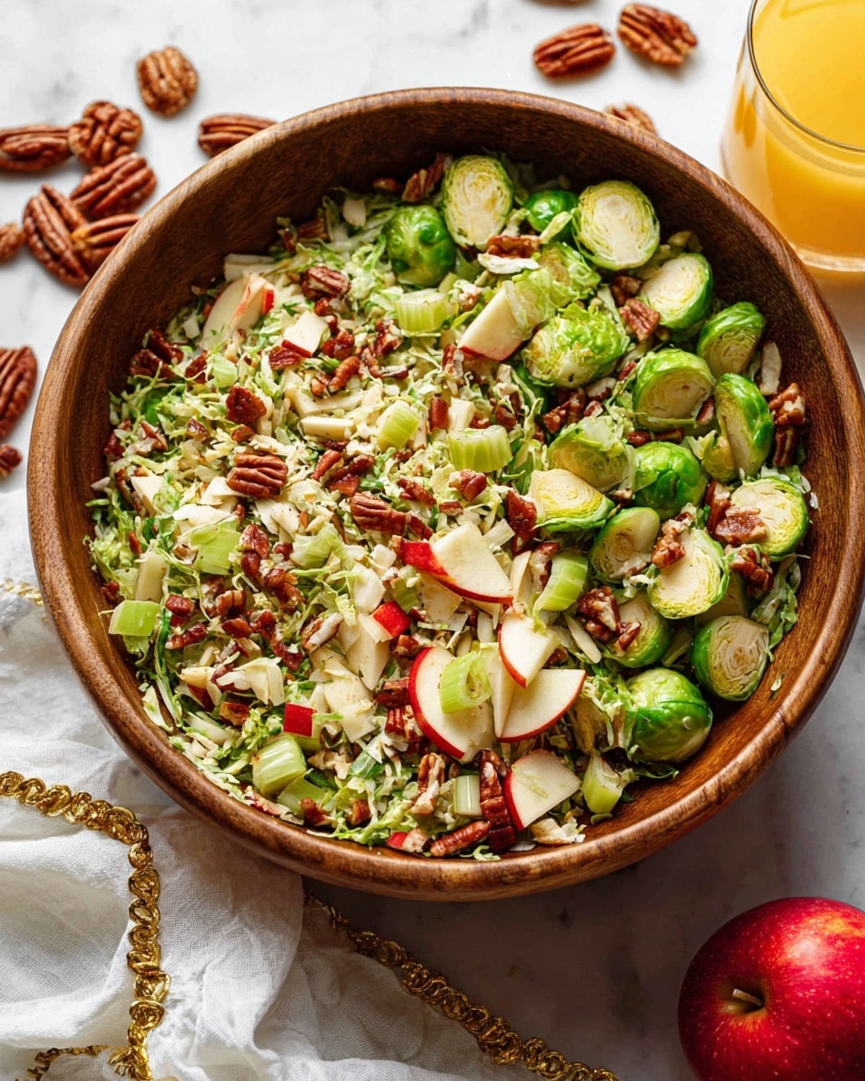 A wooden bowl filled with a fresh salad made of three main layers: the bottom layer has shredded green Brussels sprouts, the middle layer includes halved, roasted Brussels sprouts with a slight charred look, light green celery pieces, and small diced red apple chunks, and the top layer is sprinkled with broken pecan nuts and thin white cheese shavings, giving texture and contrast. The bowl sits on a white marbled surface with pecan halves and a white cloth with gold trim around it, while a glass of orange juice and a red apple are partially visible in the background photo taken with an iphone --ar 4:5 --v 7