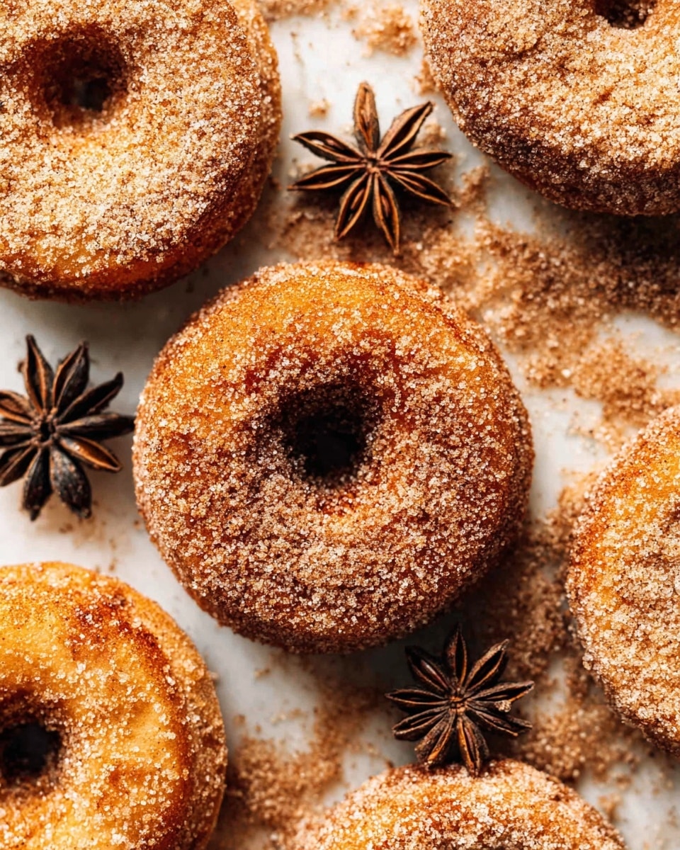 The image shows several cinnamon sugar-coated donuts close together on a white marbled surface covered with extra cinnamon sugar. Each donut is golden brown with a rough texture from the sugar coating, and they have a visible hole in the center. Near the donuts, two star anise spices are placed on the surface, adding a decorative touch. The lighting highlights the sugar granules, making them sparkle slightly. photo taken with an iphone --ar 4:5 --v 7