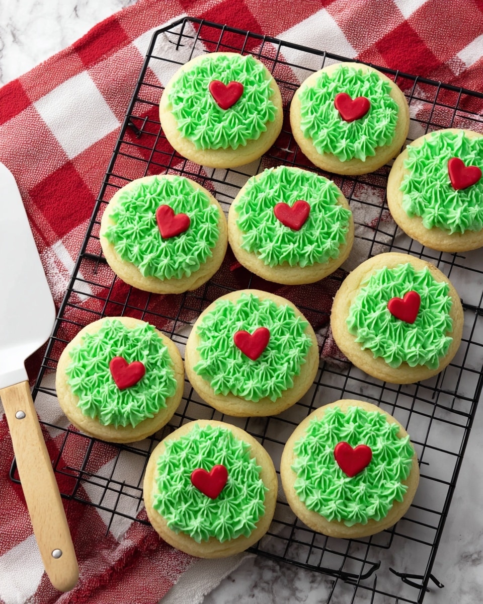 The image shows nine round sugar cookies on a black cooling rack over a white marbled surface next to a red and white checkered cloth and a white spatula with a wooden handle. Each cookie has one layer: a pale golden yellow base topped with bright green frosting piped in small star shapes covering the whole top surface, with a small red heart-shaped decoration placed slightly off-center on each cookie. Photo taken with an iphone --ar 4:5 --v 7