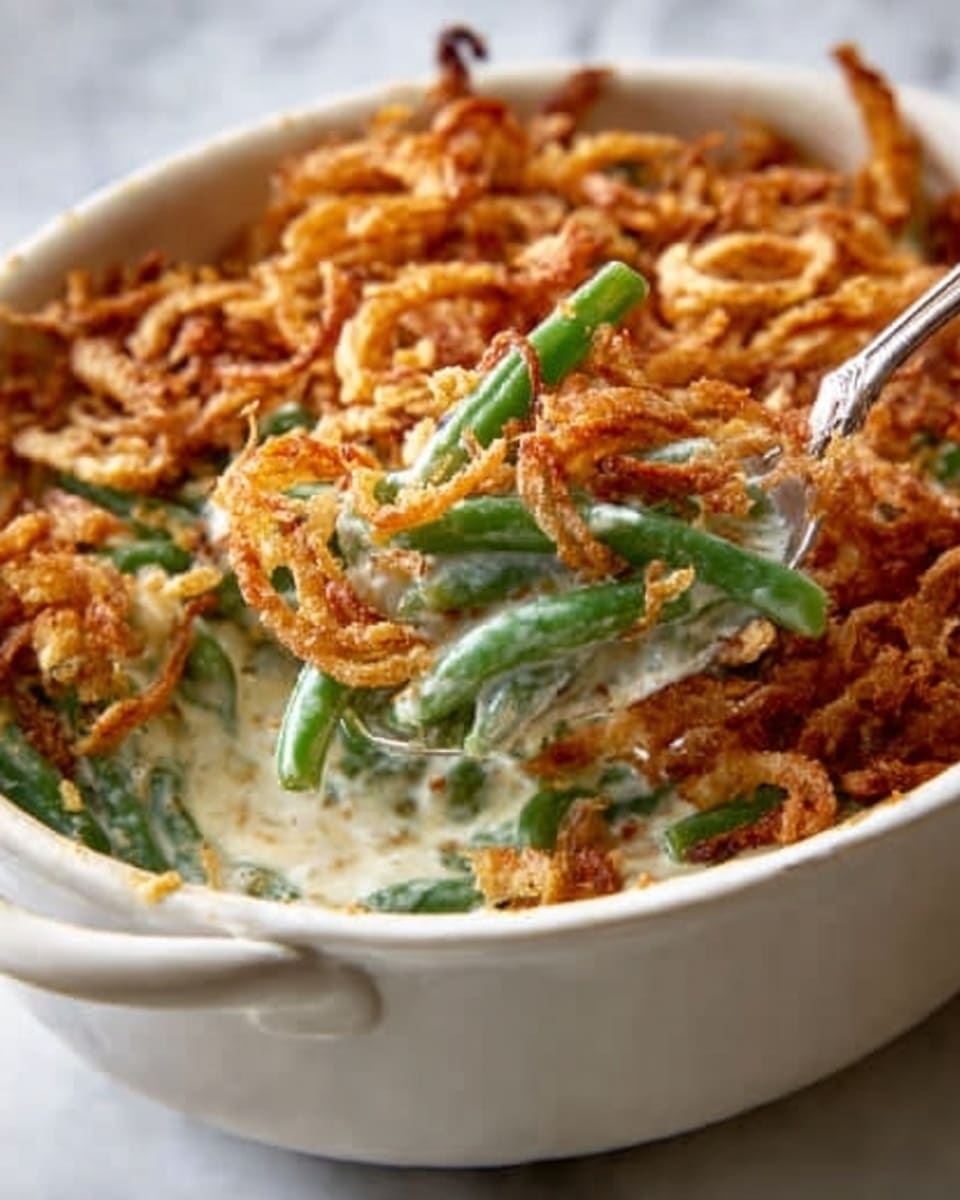 A close-up view of a green bean casserole in a dark brown oval baking dish. The dish has three visible layers: a bottom layer of creamy white sauce mixed with bright green beans, a middle layer of melted light yellow and white cheese, and a top layer of crispy, golden-brown fried onion strings spread evenly. The green beans peek through the cheese and crispy topping, showing their fresh texture. The casserole sits on a white marbled surface, and there is soft natural light highlighting the crunchy and creamy textures. photo taken with an iphone --ar 4:5 --v 7