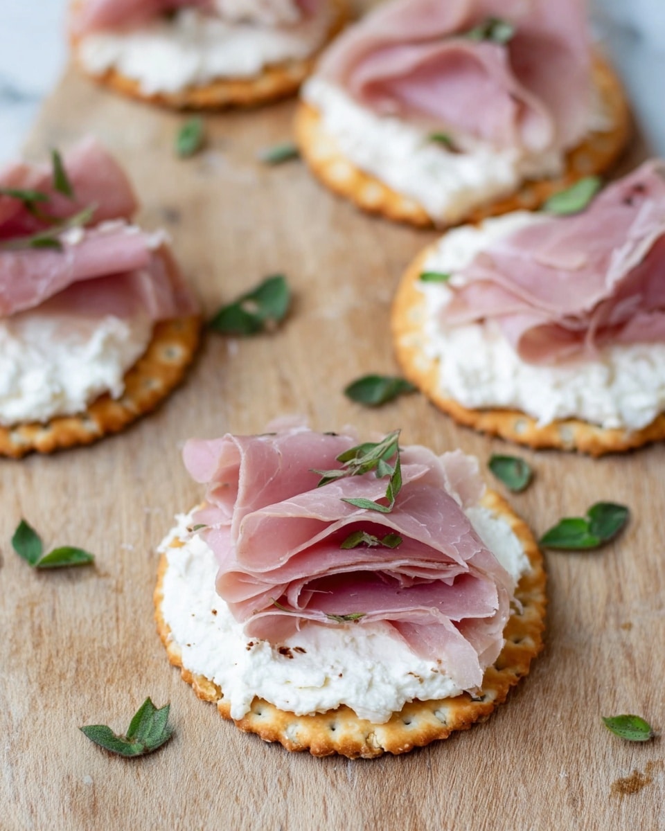 The image shows several round crackers placed on a light wood board, each cracker topped with two visible layers: the first layer is white, creamy cheese spread thickly and evenly, and the second layer is thin, folded slices of pink ham arranged loosely on top. Small green herb leaves are scattered on and around the crackers, adding a touch of color contrast. The background is a white marbled texture. photo taken with an iphone --ar 4:5 --v 7