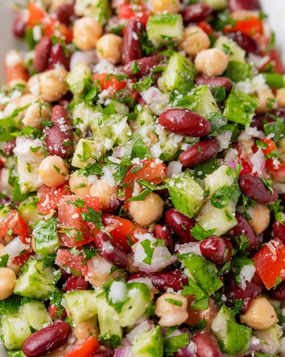 A close-up view of a fresh bean salad showing red kidney beans and light beige chickpeas mixed in evenly. There are chopped green cucumbers with a slightly glossy skin, red tomato pieces, finely chopped white onions, and leafy green parsley spread throughout. The salad is speckled with small bits of herbs and grated white cheese on top, giving a textured and colorful look. All the colors and textures are well blended, layered naturally next to and on top of each other, set on a white marbled background. photo taken with an iphone --ar 4:5 --v 7