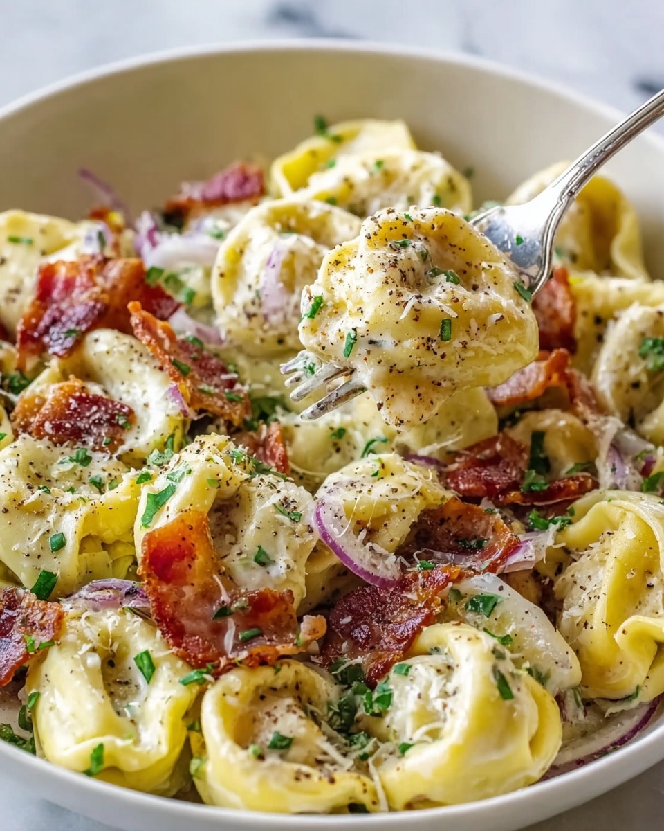 A close-up view of a white bowl filled with creamy tortellini pasta showing about two layers of pasta stuffed in yellow dough folded into ring shapes at the bottom and top. The tortellini is covered with a thick white cream sauce that coats each piece, sprinkled generously with small pieces of crispy red-brown bacon and finely grated white cheese. Green herbs are scattered throughout, adding small green dots, and thin slices of purple onion peek through the pasta. The pasta is seasoned with black pepper visible as small black specks, and a fork is lifting a piece of tortellini with bacon resting on it. The bowl is sitting on a white marbled surface. photo taken with an iphone --ar 4:5 --v 7