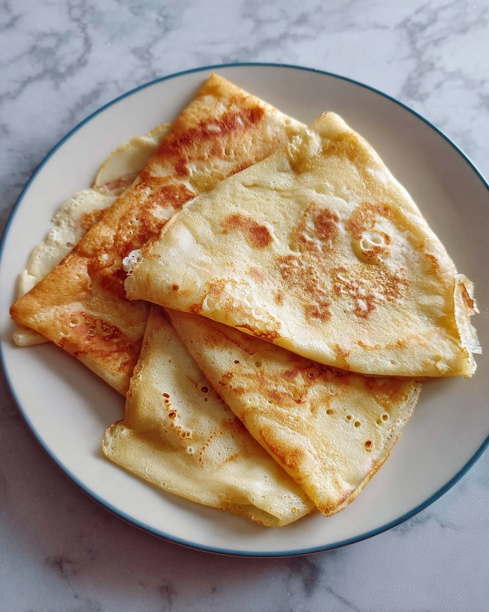 Three thin crepes are folded into quarters and placed on a white plate. The crepes show a golden brown color with some lighter spots and small bubbles on the surface, giving them a soft and slightly crispy texture. The layered crepes overlap each other slightly, showcasing both their cooked golden tops and pale undersides. The plate sits on a white marbled surface, highlighting the warm tones of the crepes. photo taken with an iphone --ar 4:5 --v 7