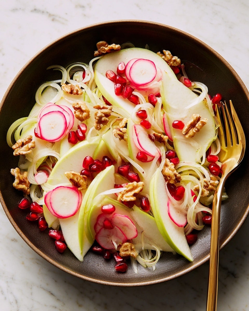 A fresh salad is shown in a dark round bowl placed on a white marbled surface. The salad has thin slices of green apple and light pink radish spread out, interspersed with translucent white onion rings and some curly pale fennel strips. Bright red pomegranate seeds and small golden brown walnut pieces are scattered on top, adding color and texture contrast. A golden fork is resting on the right side of the bowl among the salad layers. Photo taken with an iphone --ar 4:5 --v 7