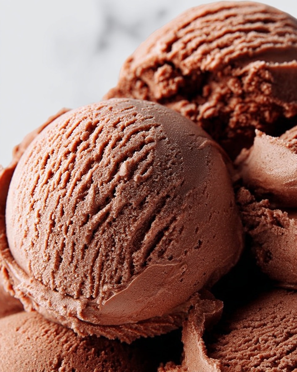 The image shows a close-up view of rich chocolate ice cream, with several scoops piled together. Each scoop has a smooth yet creamy texture, showing small ridges and fine lines from scooping. The chocolate ice cream has a deep brown color and looks soft and dense. The background is a clean white marbled texture, creating contrast with the dark ice cream. photo taken with an iphone --ar 4:5 --v 7