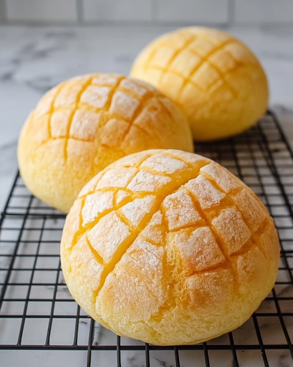 The image shows three round buns with a golden-yellow crust and a white grid pattern on top, each having a slightly puffed texture. The buns have a soft, irregular surface with small cracks in the crust, highlighting their freshly baked feel. They are placed on a black wire cooling rack that sits on a white marbled surface. The buns are arranged in a triangular shape, with one bun in the foreground and two behind it, creating a sense of depth. Photo taken with an iphone --ar 4:5 --v 7